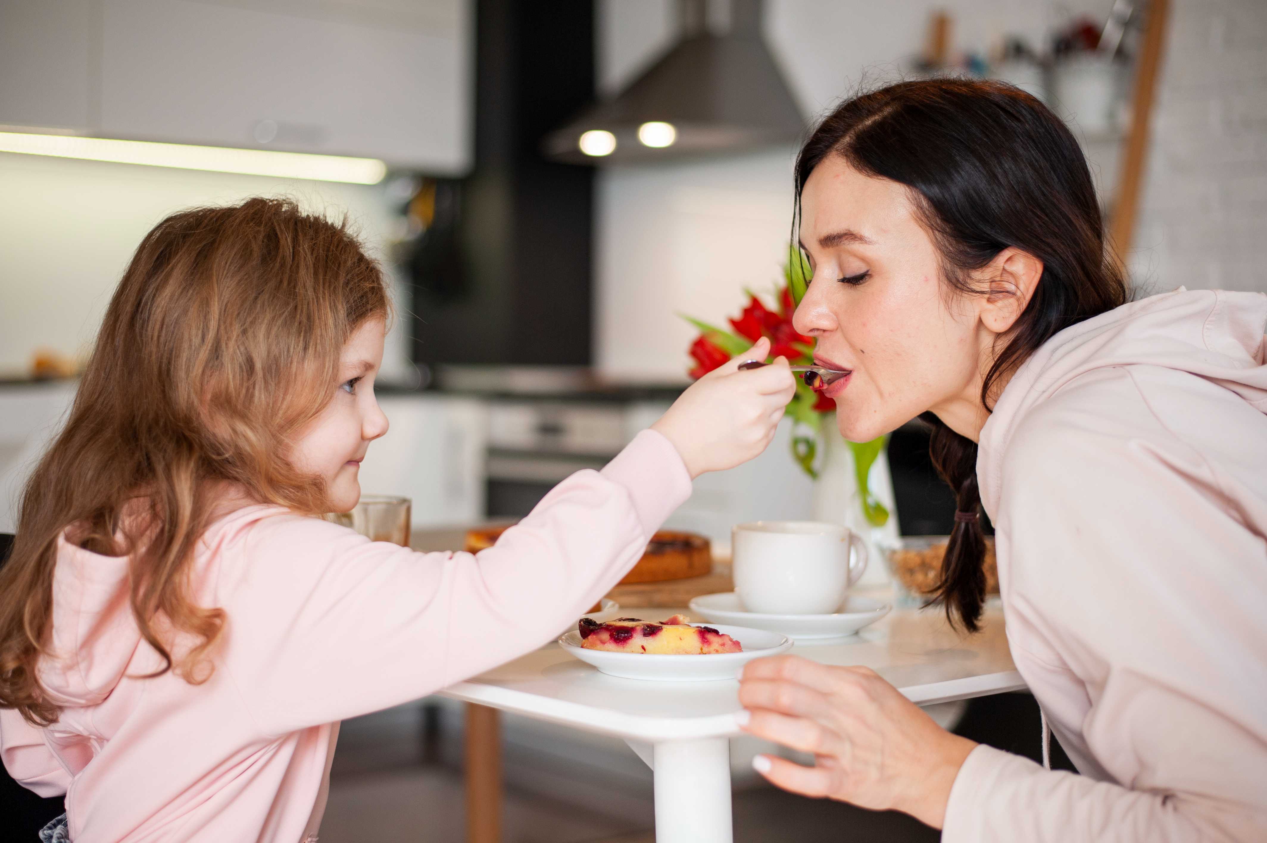 Mother and daughter sharing dessert, girl feeding mom with a spoon.