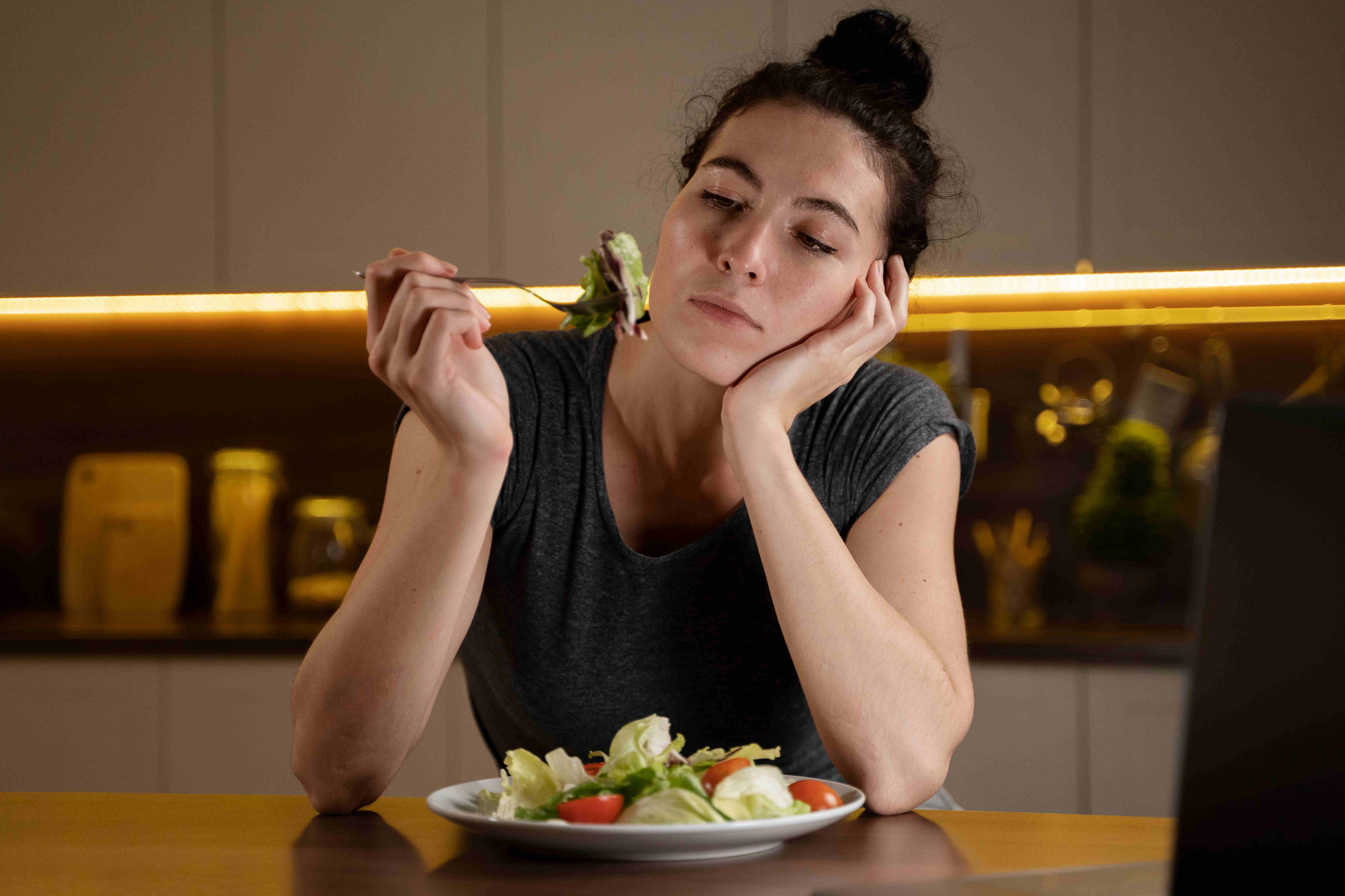 Tired woman staring at a plate of salad with low enthusiasm, highlighting the conflict between healthy intentions and emotional disinterest in food after childbirth.