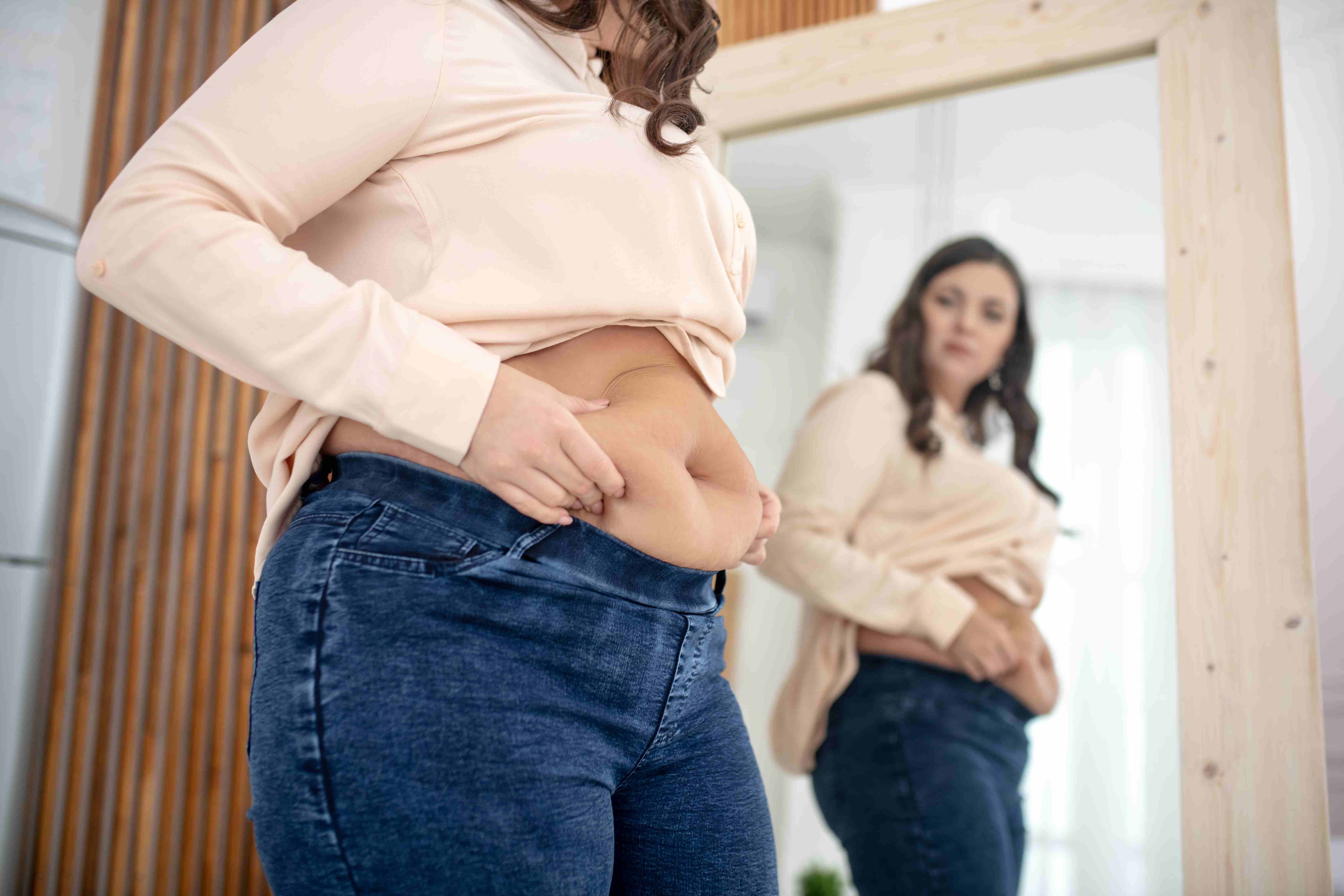 New mother in postpartum, looking at her belly in the mirror while adjusting tight jeans