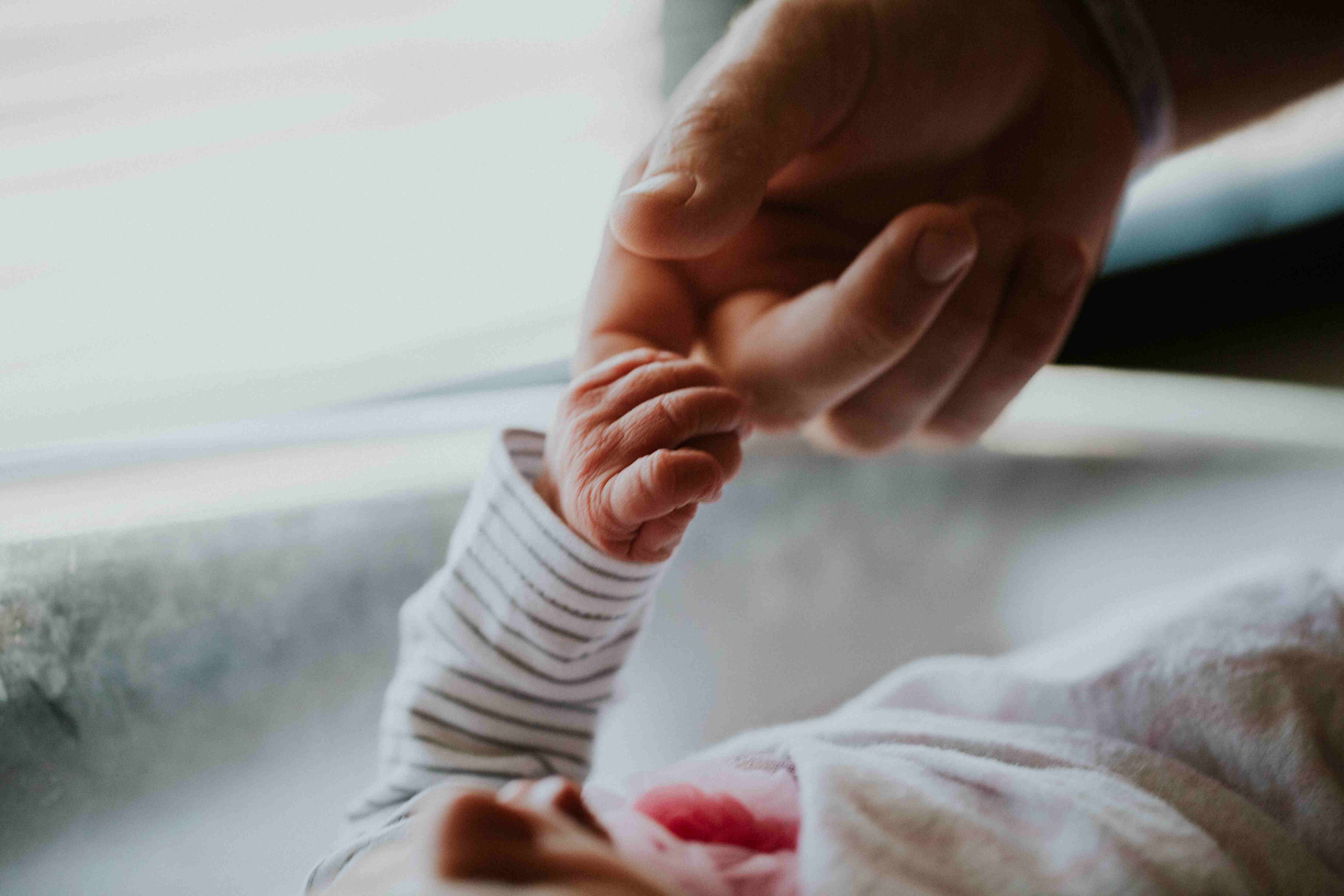 Close-up of a newborn baby’s tiny hand holding their parent’s finger.