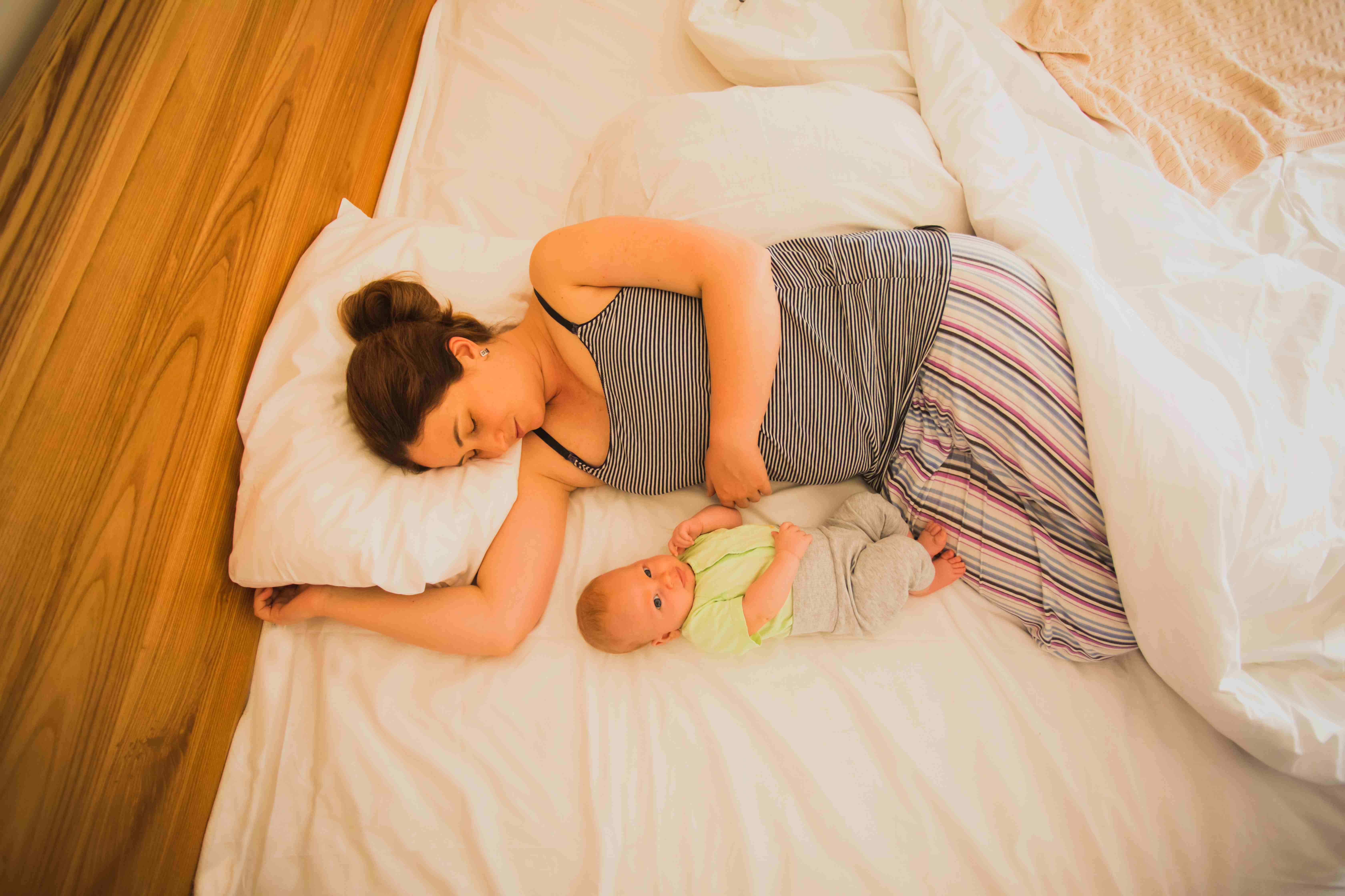 New mom is peacefully in light, breathable clothes, relieving herself from night sweats. She is sleeping beside her newborn, both relaxed in bed.