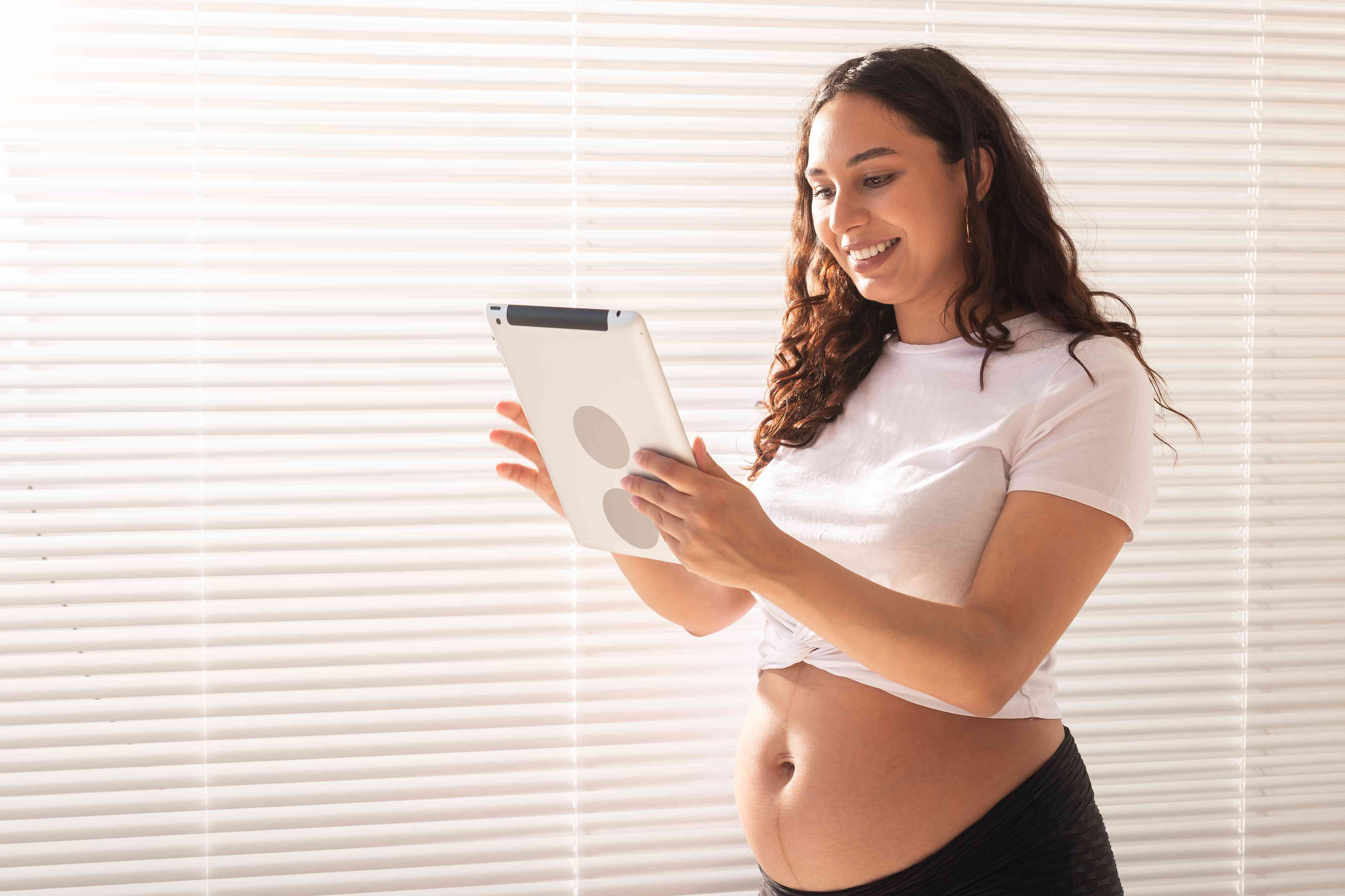 Happy postpartum woman video chatting using tablet, smiling and relaxed in casual clothing